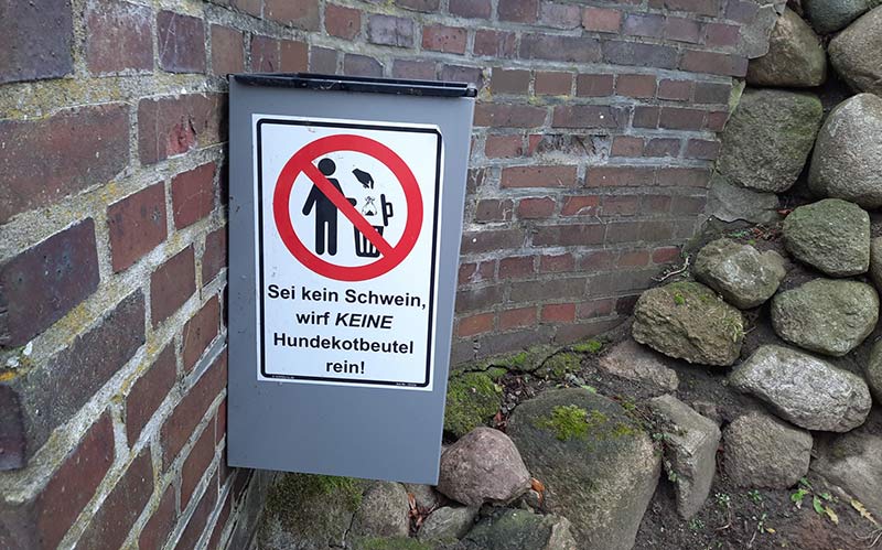 Aufkleber "Sei kein Schwein, wird KEINE Hundekotbeutel rein!" am Mülleimer.