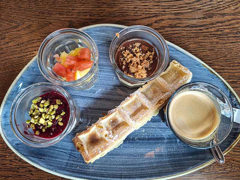 Café gourmand, der Kaffee Vielfraß, serviert mit dreielei Dessert im Gläschen und Waffel.